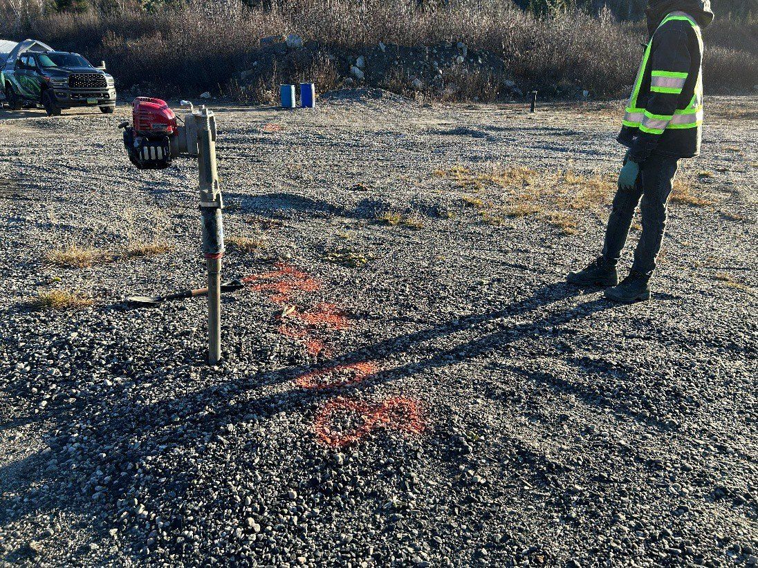 Tarière manuelle motorisée plantée dans un sol de gravier, à côté d’un technicien
