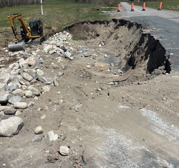 Chaussée effondrée par le glissement du talus, route fermée par des cônes et pelle mécanique sur place